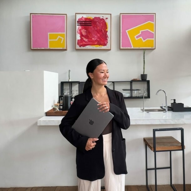 Eine lächelnde Frau mit Laptop unter dem Arm steht vor einer modernen Küchenzeile mit abstrakten Gemälden in einem Loft.