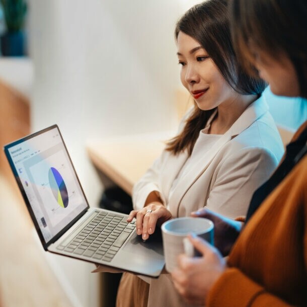 Zwei Frauen schauen gemeinsam auf einen Laptop, dessen Bildschirm ein Tortendiagramm zeigt.