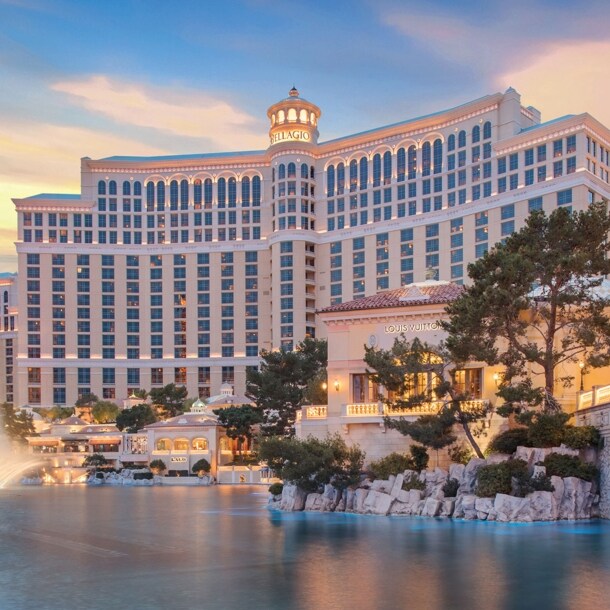 Prunkvoller Hotelkomplex hinter einem künstlichem See mit beleuchteter Wasserfontäne bei Sonnenuntergang.