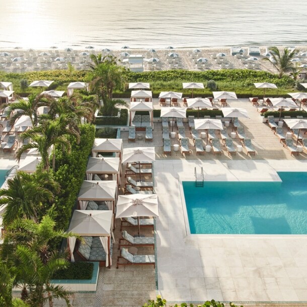 Hotelterrasse mit Palmen und Liegen am Pool an einem weißen Sandstrand mit weiteren Liegen.