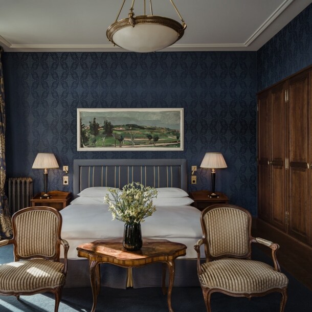 Gemütliches Hotelzimmer mit Doppelbett vor dunkelblauer Tapete und großem Holzkleiderschrank.