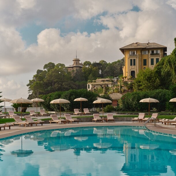 Luxuriöse Hotelterrasse mit Pool und Liegestühlen an einer mediterranen Küste.