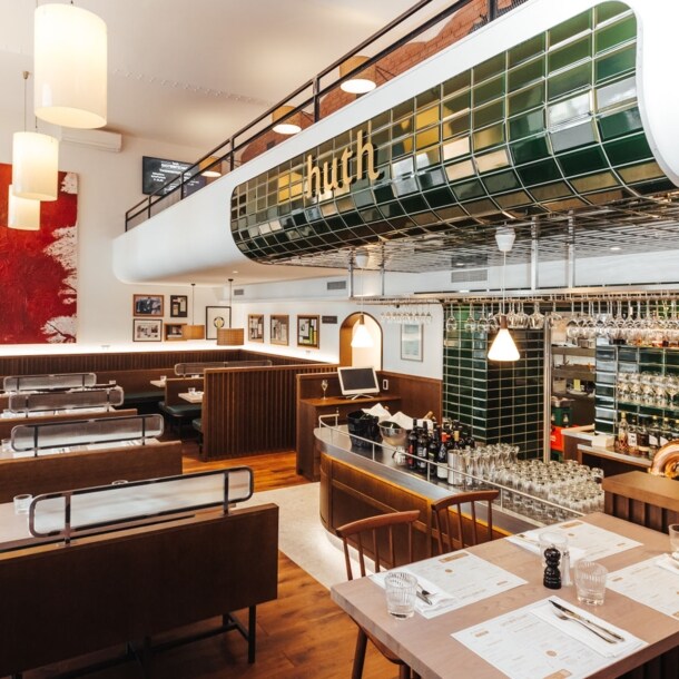 Moderner Speiseraum mit Holzmobiliar und Barbereich mit grünen Kacheln mit der Aufschrift huth.