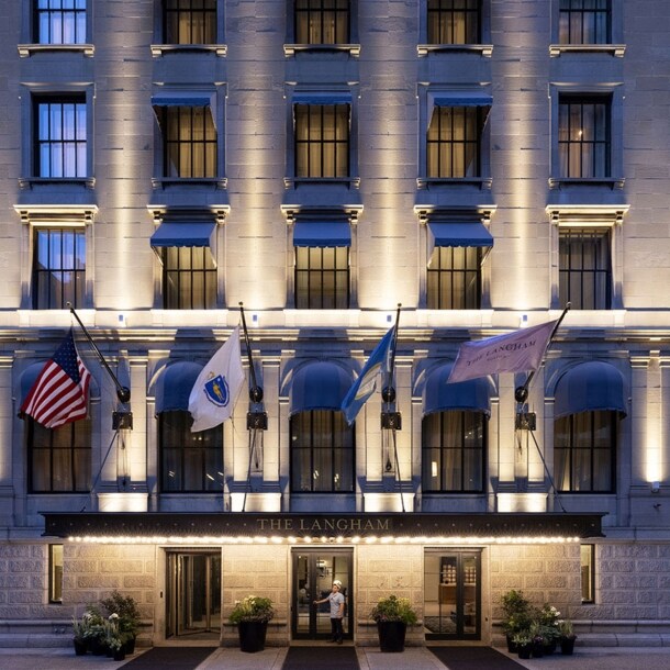 Beleuchtete Fassade eines Luxushotels mit wehenden Fahnen über dem Eingangsbereich.