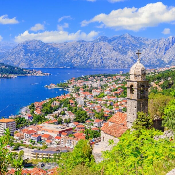 Blick auf die Stadt Kotor mit Häusern und Kirchturm, im Hintergrund Berge und eine Bucht.