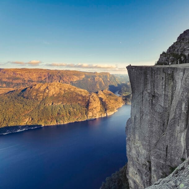 Fjordlandschaft an einem klaren Tag mit Personen auf einer beeindruckenden Felsklippe.