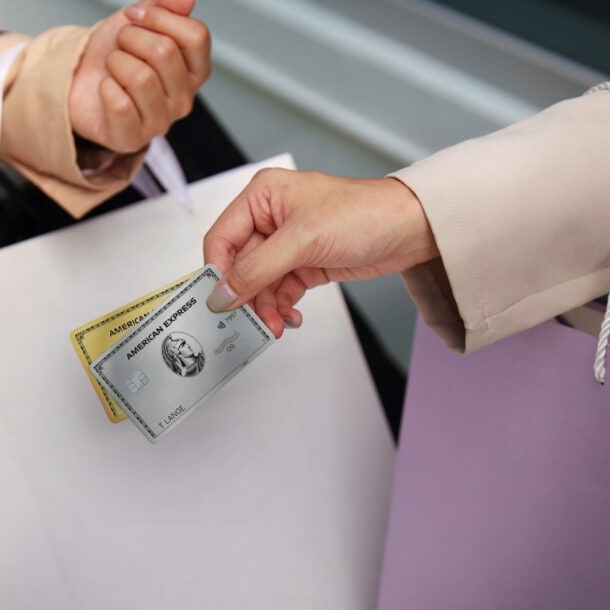 Nahaufnahme von zwei Armen mit Einkaufstüten, eine Hand hält eine goldene und eine silberne Kreditkarte von American Express.