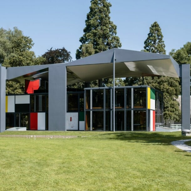 Eine Familie läuft auf ein modernes, fragmentiertes Gebäude im Le Corbusier-Stil in einer Parkanlage zu.