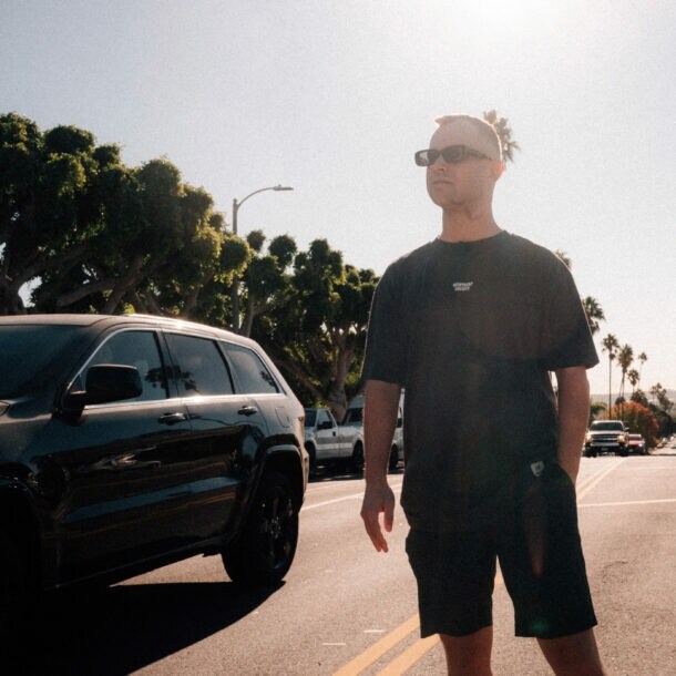 Benjamin Diedering posiert mit Sonnenbrille auf einer palmengesäumten Straße bei Sonnenschein.