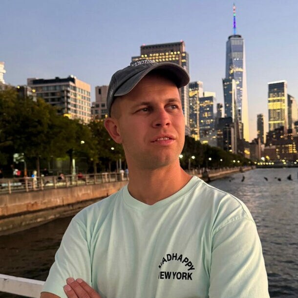 Porträt von Benjamin Diedering mit Baseballcap vor der Skyline New Yorks am Wasser.