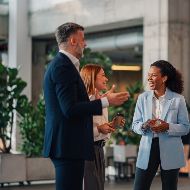Zwei Frauen und zwei Männer in Business-Kleidung stehen beieinander und kommunizieren lächelnd in einem Foyer.