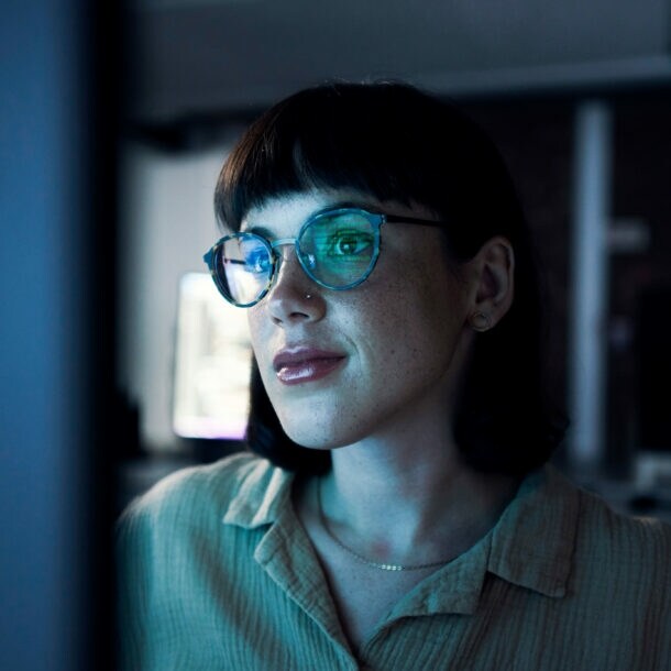 Eine Frau mit einer Brille in einem dunklen Raum vor einem Bildschirm.