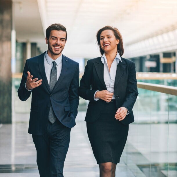 Ein Mann und eine Frau in formeller Business-Kleidung kommunizieren nebeneinander gehend.