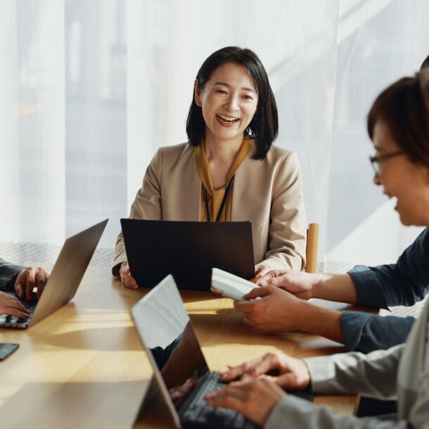 Eine Gruppe asiatischer Menschen sitzt lächelnd mit Laptops an einem Tisch.