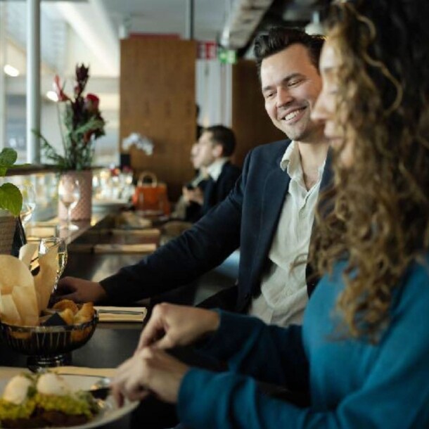 Ein Mann und eine Frau beim Essen an einem Fensterplatz in einer Flughafen-Lounge.