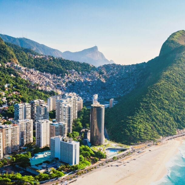 An einem Strand liegt eine Stadt mit Hochhäusern und riesigen Bergen.