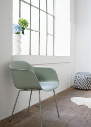 Ein grüner Stuhl aus Plastik steht an einer Wand neben einem Fenster