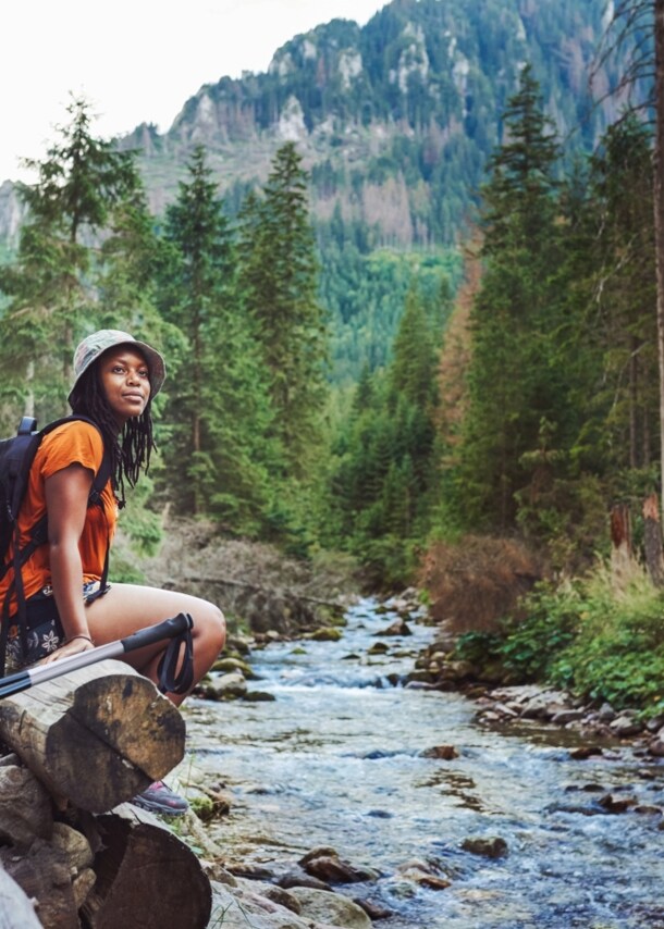Eine Frau sitzt mit Wanderausrüstung an einem Bach im Wald