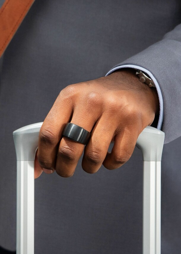 Ein Smart Ring am Mittelfinger einer Hand, die einen Trolley hält