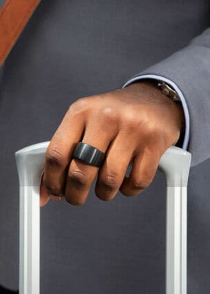Ein Smart Ring am Mittelfinger einer Hand, die einen Trolley hält