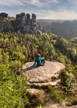 Eine Frau auf einer Felsenplattform, die auf die Sächsische Schweiz blickt