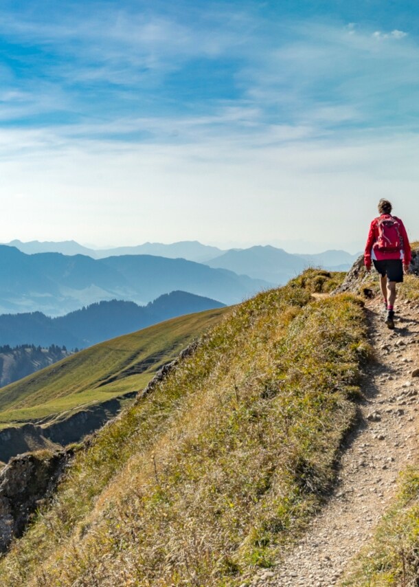 Rückansicht einer Person mit rotem Rucksack auf einem Wanderweg in den Bergen