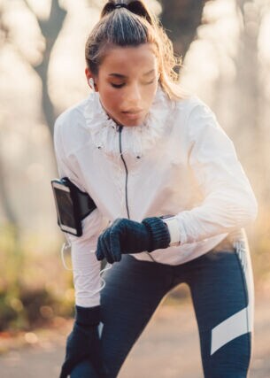 Eine Frau im Joggingdress blickt nach dem Laufen auf ihre Smartwatch