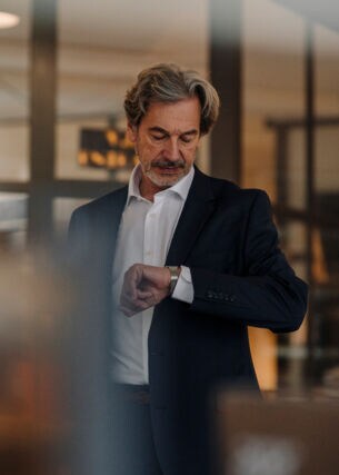 Ein Mann in Anzug schaut auf seine Armbanduhr