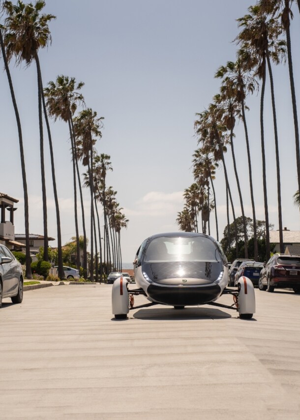 Ein futuristisches Fahrzeug fährt in der Sonne auf palmengesäumter Straße