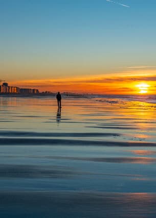 Eine Person am Strand bei Sonnenuntergang vor einer Stadt im Hintergrund