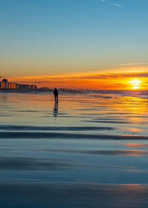Eine Person am Strand bei Sonnenuntergang vor einer Stadt im Hintergrund