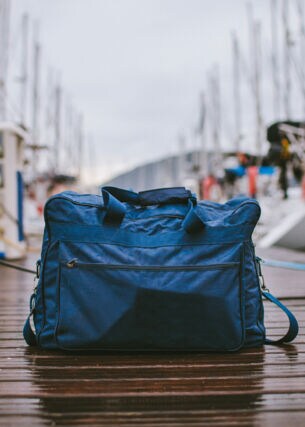 Eine gepackte Reisetasche steht auf einem Anlegeplatz für Segelboote