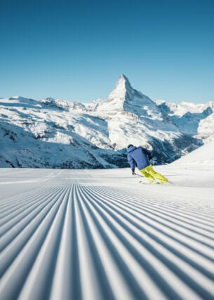 Ein Skifahrer fährt eine perfekt präparierte Piste hinunter, mit Blick auf das Matterhorn