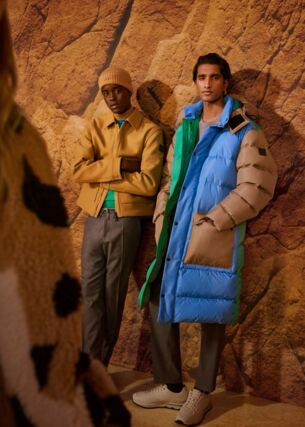 Zwei männliche und weibliche Models lehnen an einer ockerfarbenen Felswand und tragen winterliche Outfits aus der FW Kollektion von BOSS