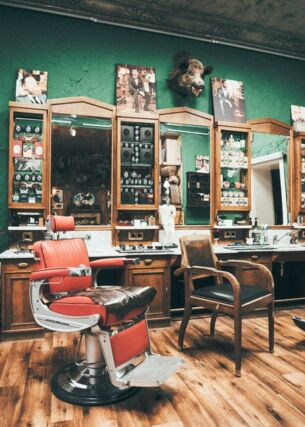 Das Interieur eines Vintage-Barbershops mit dunkelgrünen Wänden, Ledersofa und Retro-Friseurstühlen