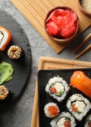 Aufsicht unterschiedlicher Sushi-Sorten auf zwei Tellern, daneben Beilagen und Stäbchen