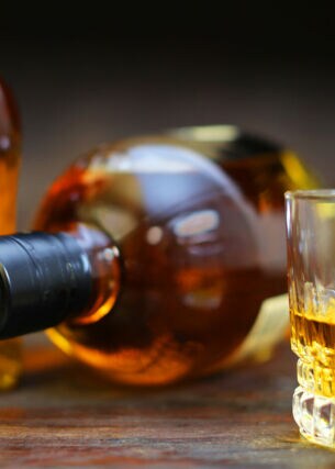Ein Glas mit Whisky vor einer stehenden und einer liegenden Flasche auf einem Tisch