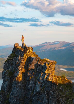 Eine Wanderin auf einem Felsen an einem Fjord.