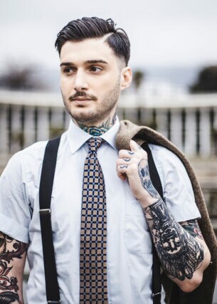 Ein junger Mann mit Tattoos trägt Hosenträger und Krawatte.