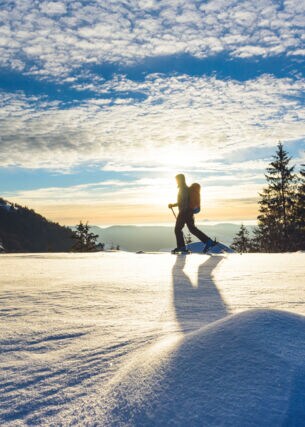Eine Frau läuft auf einer Loipe mit Blick in die Berglandschaft in der Wintersonne