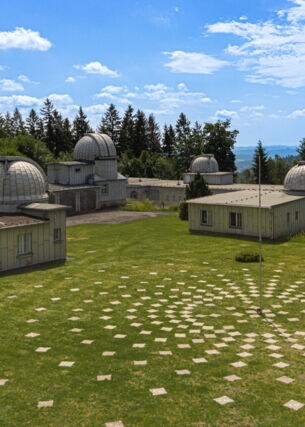 Gelände der Sternwarte Sonneberg, auf dem sich mehrere Gebäude mit Kuppeln befinden, daneben eine Installation mit Markierungssteinen, die sich kreisförmig am Boden um eine Stange anordnen