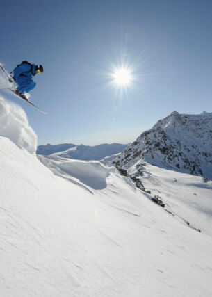 Skifahrer:in springt von einer Klippe, Sonne und Schnee