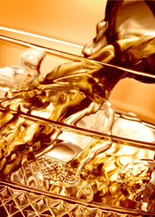 In ein Whiskyglas wird Flüssigkeit aus einem Flaschenhals gegossen, Nahaufnahme mit goldener Bildtonung