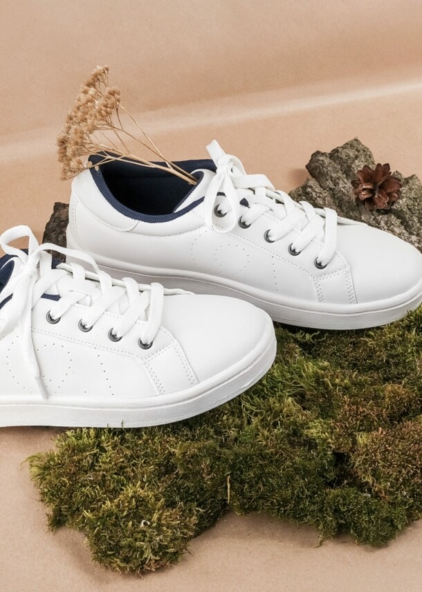 Ein Paar weiße Turnschuhe mit trockenen Blumen auf Baumrinde und Moos