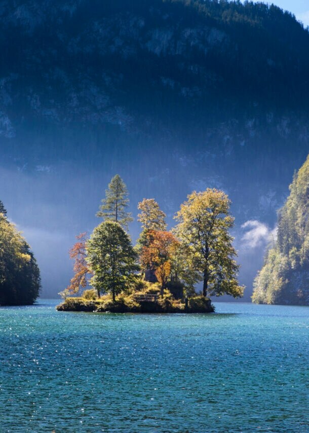 Ein großer See mit einer Insel mit herbstlichen Laubbäumen, eingebettet von riesigen Felswänden
