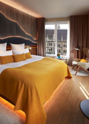 Modernes, stilvolles Hotelzimmer mit großem Doppelbett und Blick auf den Münchener Marienplatz
