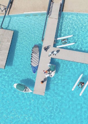 Ein großer Pool mit hellblauem, klaren Wasser sowie Booten, Katamaranen und zwei geometrischen hellgrauen Stegen in Betonoptik