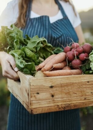 Eine junge Frau trägt eine Kiste mit frischem Gemüse.