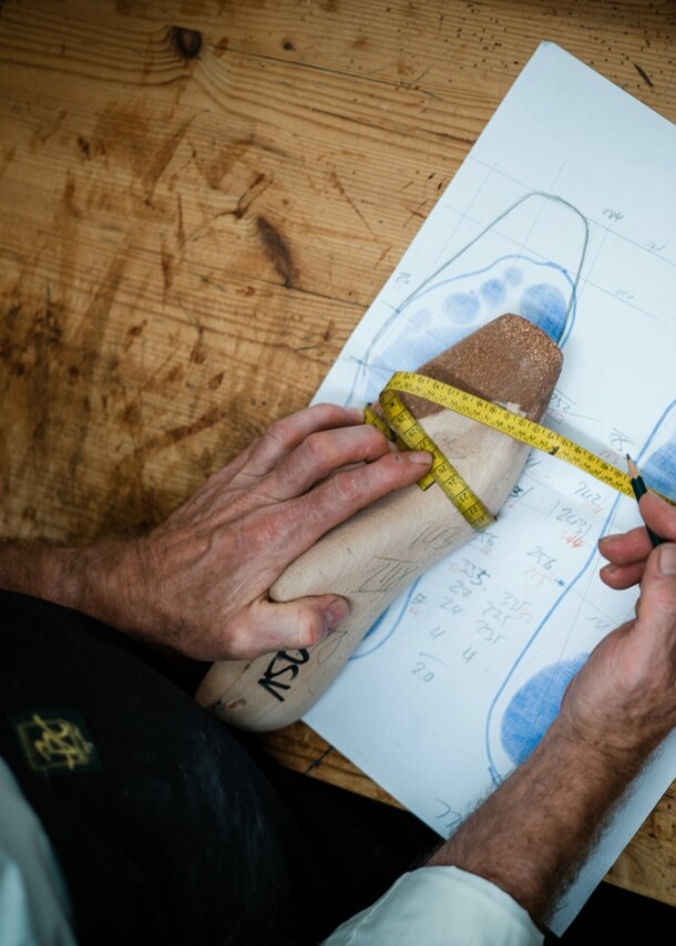 Ein Schuster misst anhand eines Modells die Fußbreite.