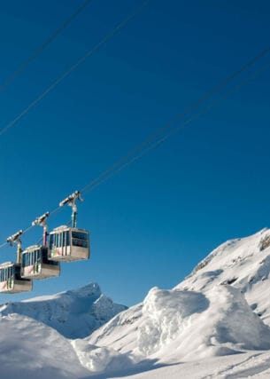 Eine Seilbahn vor blauem Himmel und schneebedeckten Bergen